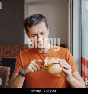 Un uomo accigliato cliente di un fast food scava in un hamburger e ha trovato un prodotto guastato nel suo pranzo Foto Stock
