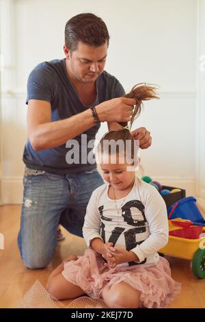 Prendendosi cura del suo piccolo angelo, un padre che piega i capelli delle sue figlie a casa. Foto Stock