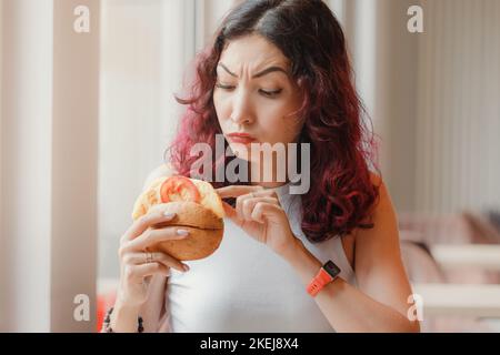 Una ragazza scontenta cliente di un fast food ristorante scava in un hamburger e ha trovato un prodotto guastato nel suo pranzo Foto Stock