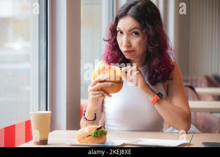 Una ragazza frowned scontentata cliente di un fast food ristorante scava in un hamburger e ha trovato un prodotto guastato nel suo pranzo Foto Stock