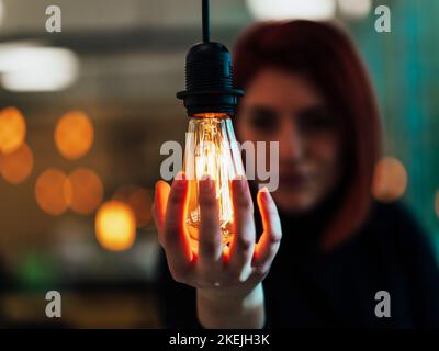 Foto simbolica di una donna d'affari che tiene una lampadina in un ufficio moderno Foto Stock