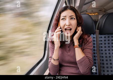 Una ragazza infastidita viaggia su un treno e, a causa del rumore e di un segnale cattivo, non riesce a sentire l'interlocutore. Scarsa copertura della rete cellulare Foto Stock
