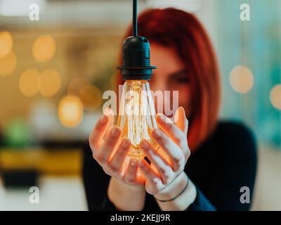 Foto simbolica di una donna d'affari che tiene una lampadina in un ufficio moderno Foto Stock