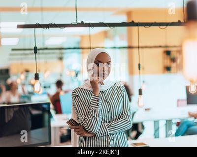 Protarit di una donna musulmana nera (afro-americana) in piedi in un moderno ufficio d'affari mentre indossa un hijab. Foto Stock