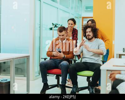 Team building e divertimento in ufficio. Giovane uomo d'affari allegro in abbigliamento casual elegante che si diverte mentre gareggiare su sedie da ufficio e sorridendo. Foto Stock