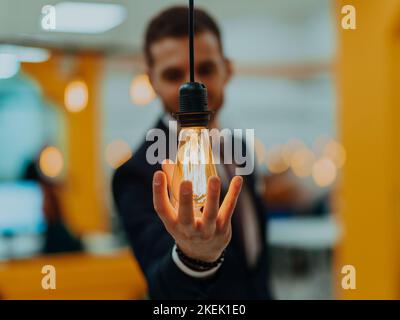 Foto simbolica di un uomo d'affari che tiene in mano una lampadina in un ufficio moderno Foto Stock
