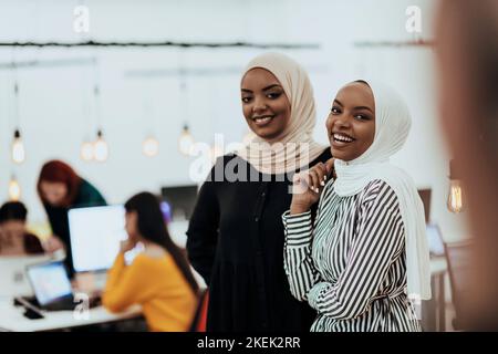 Ritratto di due donne d'affari afroamericane che parlano tra loro mentre si trovano in un moderno ufficio commerciale con i loro colleghi. Marketing Foto Stock