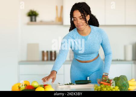 Giovane ragazza sportiva afro-americana che taglia il cetriolo e prende il peperone, prepara insalata di verdure fresche, copia spazio Foto Stock