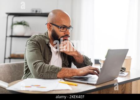 Ritratto di un dipendente maschile concentrato che lavora su un computer portatile alla scrivania dell'ufficio di casa, controllando il progetto online, copiando lo spazio Foto Stock