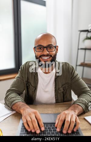 Positivo uomo maturo freelancer scrivere sul notebook e guardare lo schermo, pov ripresa di un uomo latino che lavora a casa ufficio Foto Stock