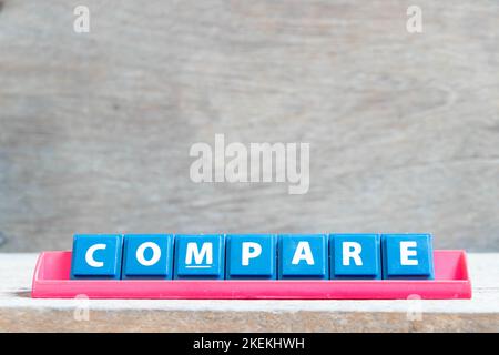 Lettera dell'alfabeto della piastrella con la parola confronta in rack di colore rosso su sfondo di legno Foto Stock