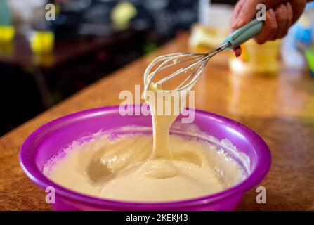 Processo di cottura delle frittelle fatte in casa: Mescolare la farina, il latte e gli ingredienti delle uova in un recipiente con una frusta Foto Stock