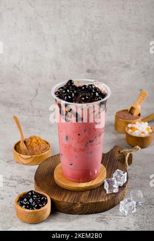 Le perle di Boba o tapioca sono il tè del latte della bolla di taiwan in tazza di plastica con sapore di velluto rosso su fondo di consistenza, rinfresco estivo. Foto Stock