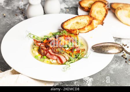 Chiudere la zuppa di piselli in un recipiente bianco. Deliziosa zuppa di verdure con piselli verdi, carote e pancetta fritta. Foto Stock