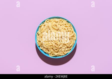 Vista sopra con una porzione di pasta cacio e pepe, minimalista su un tavolo viola. Delizioso piatto italiano, spaghetti con formaggio grattugiato e pepa nera Foto Stock