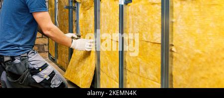 casa muro isolamento. costruzione lavoratore installare lana di vetro nel profilo di metallo telaio indoor. banner con spazio copia Foto Stock