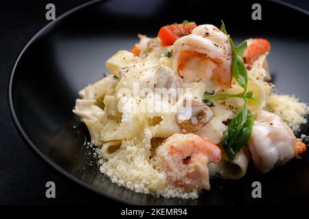 Pasta con gamberi, formaggi, funghi e verdure su fondo scuro Foto Stock