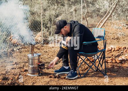 Uomo che illumina samovar per tè, caffè, acqua calda nel campo. Foto Stock