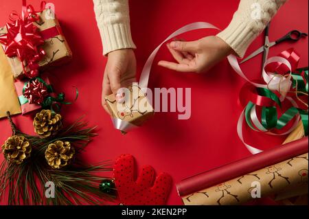 Direttamente sopra, le mani della donna che avvolgono un piccolo regalo in una carta regalo con motivo del cervo, legare in su usando un nastro bianco Foto Stock