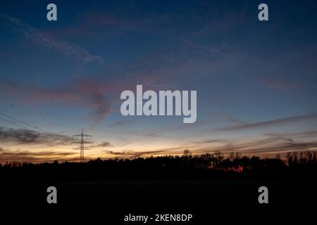 Bella e spettacolare nuvola arancione e blu e cielo dopo la tempesta e piovere su campo agricolo e alta tensione torre sulla campagna in Germania. Foto Stock