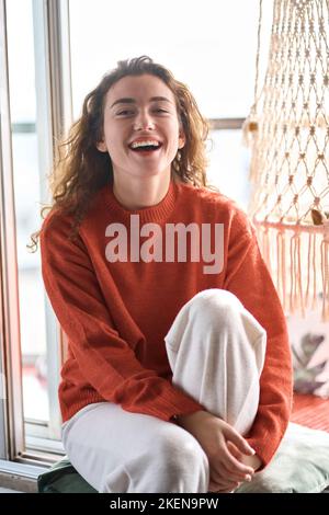 Felice giovane donna seduta sul windowsill a casa e ridendo. Foto Stock