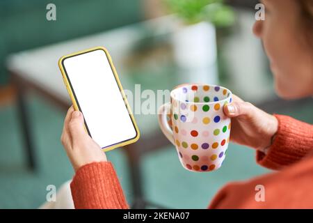 Donna che tiene lo smartphone bianco mock up schermo e caffè, a spalla. Foto Stock