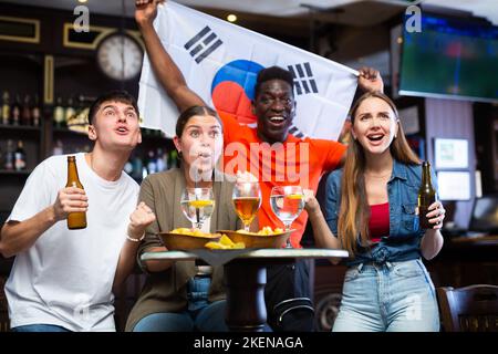 Un gruppo di tifosi felici festeggia la vittoria della loro squadra preferita con la bandiera della Corea del Sud nel bar della birra Foto Stock