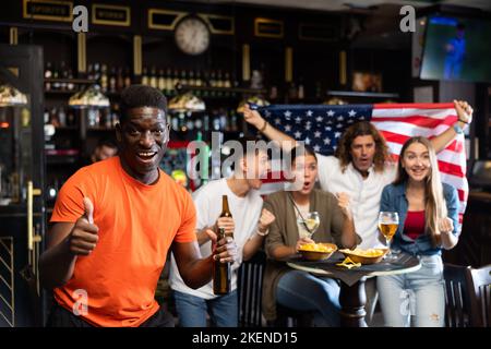 Un entusiasta uomo africano che fa il tifo per la squadra di baseball americana preferita nel bar dello sport Foto Stock