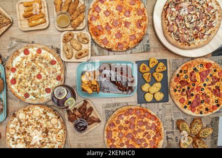 Set di fast food e pizze di famiglia con quattro formaggi appena sfornati, costolette alla griglia, ali di pollo con salsa di bufalo e pane all'aglio Foto Stock