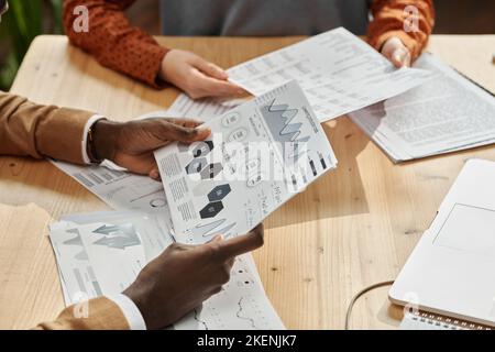 Primo piano dei colleghi che discutono insieme i grafici finanziari a un tavolo di legno in ufficio Foto Stock