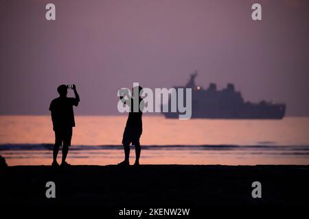 Nusa Dua, Indonesia. 14th Nov 2022. Due uomini scattano una foto davanti ad una nave della Marina Indonesiana sulla spiaggia di Nusa Dua prima dell'alba il giorno prima dell'inizio della vetta del G20. L'incontro del gruppo G20, i paesi industrializzati più forti e le economie emergenti, si terrà il 15 e 16 novembre. Credit: Christoph Soeder/dpa/Alamy Live News Foto Stock