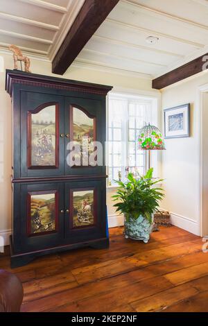 Antico armadio in legno con scene dipinte sulle porte e lampada tiffany a piedistallo nel soggiorno all'interno di una vecchia casa ricostruita in stile canadese del 1886. Foto Stock