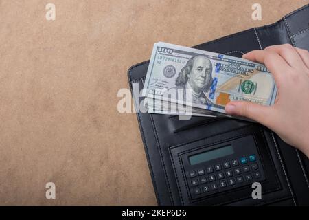 Mano che tiene le banconote del dollaro americano sulla calcolatrice Foto Stock
