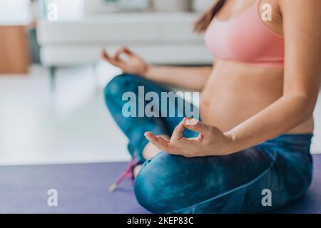 Yoga prenatale. Donna incinta che fa meditazione. Donna meditando durante la gravidanza a casa sul tappetino del pavimento in posizione lotus esercizio di respirazione Foto Stock