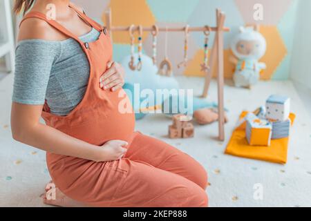 Pancia donna incinta con attività di baby gym gioco, giocattoli e tappetino per bambini in asilo nido o sala giochi. Concetto di gravidanza e pianificazione e decorazione casa nusery Foto Stock