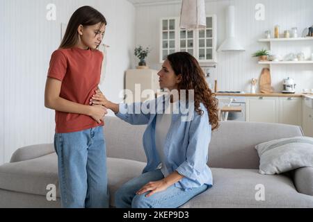 Ragazza adolescente bambino lamentarsi di stomachache a madre a casa. Adolescenti e dolore mestruale Foto Stock