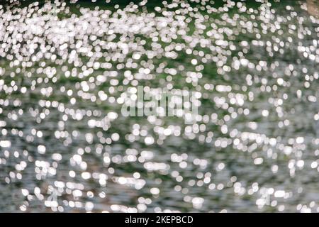 Superficie dell'acqua sfocata con riflessi solari, sfondo astratto, riflessione sull'acqua, giorno di sole Foto Stock