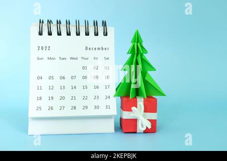 Focalizzazione selettiva del calendario da tavolo di dicembre 2022 su sfondo blu con albero di natale, regalo e spazio copia. Foto Stock