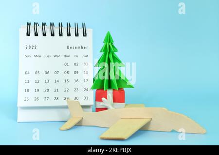 Focus selettivo del calendario da tavolo di dicembre 2022 con modello di aereo e albero di natale su sfondo blu. Vacanze natalizie e viaggi di vacanza Foto Stock