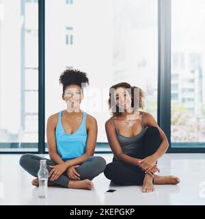 Fare una piccola pausa. Ritratto di due giovani donne in forma seduto sul pavimento e facendo una chiacchierata prima di una sessione di yoga all'interno di uno studio. Foto Stock