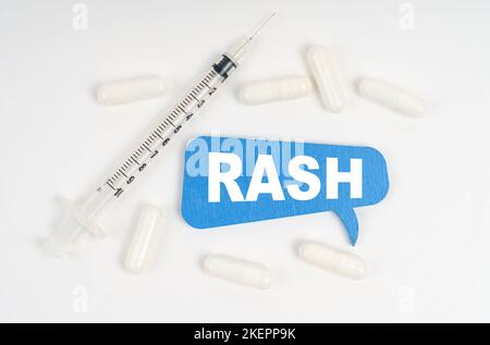 Medicina e concetto di salute. Su uno sfondo bianco pillole, una siringa e una piastra blu con l'iscrizione - eruzione cutanea Foto Stock