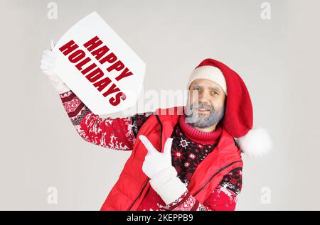 Concetto di Natale. Babbo Natale tiene un segno con l'iscrizione nelle sue mani - BUONE FESTE e gli indica con l'altra mano Foto Stock