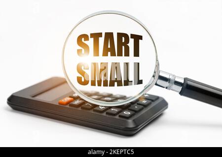 Concetto di business e finanza. Sulla tabella si trova una calcolatrice e una lente d'ingrandimento, all'interno della quale l'iscrizione - Start Small Foto Stock