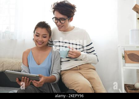 Allegra coppia vietnamita che legge qualcosa sul computer tablet Foto Stock