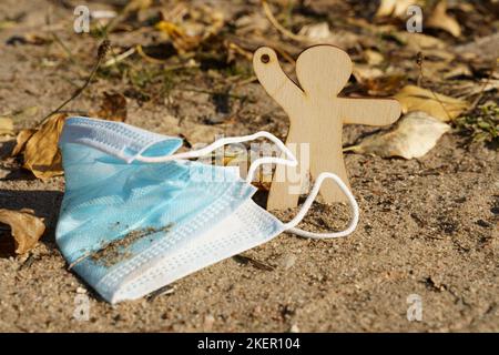 Concetto ambientale. La figurina mans richiama l'attenzione sulla maschera medica che giace a terra. Foto Stock