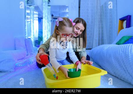 Bambino con disabilità fisica in sala stimolante sensoriale, snoezelen. Bambino che vive con la paralisi cerebrale interagendo con il suo terapeuta durante la terapia Foto Stock