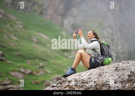 Trekker scatta foto con lo smartphone seduto in montagna Foto Stock