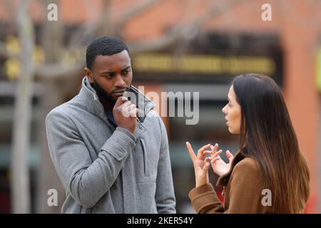 Uomo sospettoso che ascolta una donna che parla in inverno per strada Foto Stock