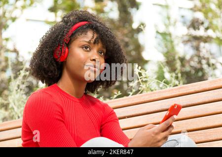 giovane donna seduta su una panchina che ascolta la musica con le cuffie che esprimono la fiducia in se stessi all'aperto Foto Stock