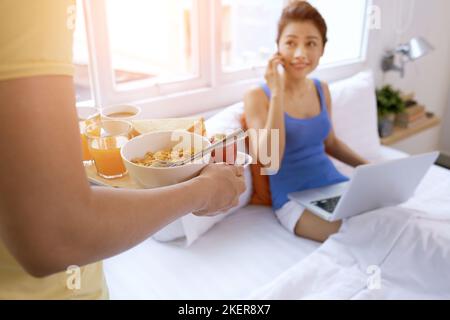 Uomo che porta gustosa colazione a letto alla sua ragazza Foto Stock